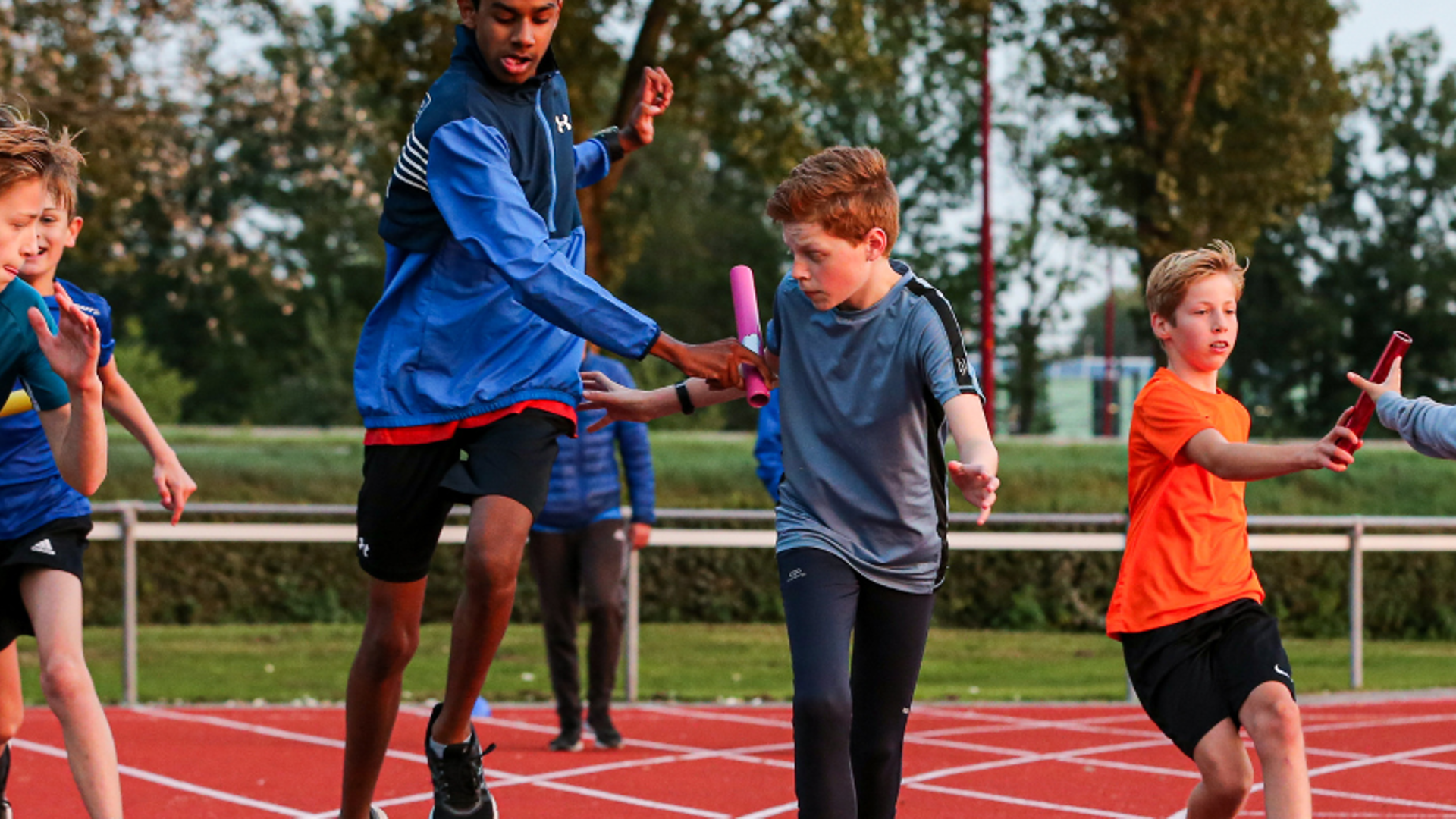 vijf sportende kinderen op een atletiekbaan