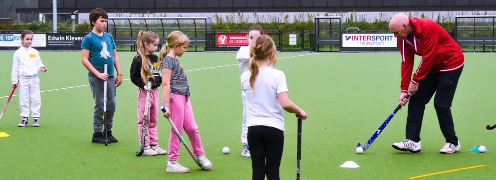 Kinderen die een hockeytraining krijgen van een volwassen meneer